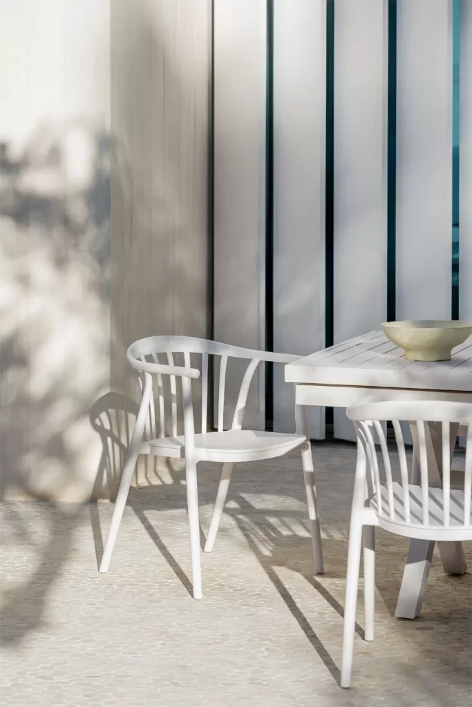 Mobilier blanc minimaliste sur une grande terrasse avec une table et des chaises d'extérieur, un exemple de la façon de décorer de grandes terrasses dans un style moderne et fonctionnel.