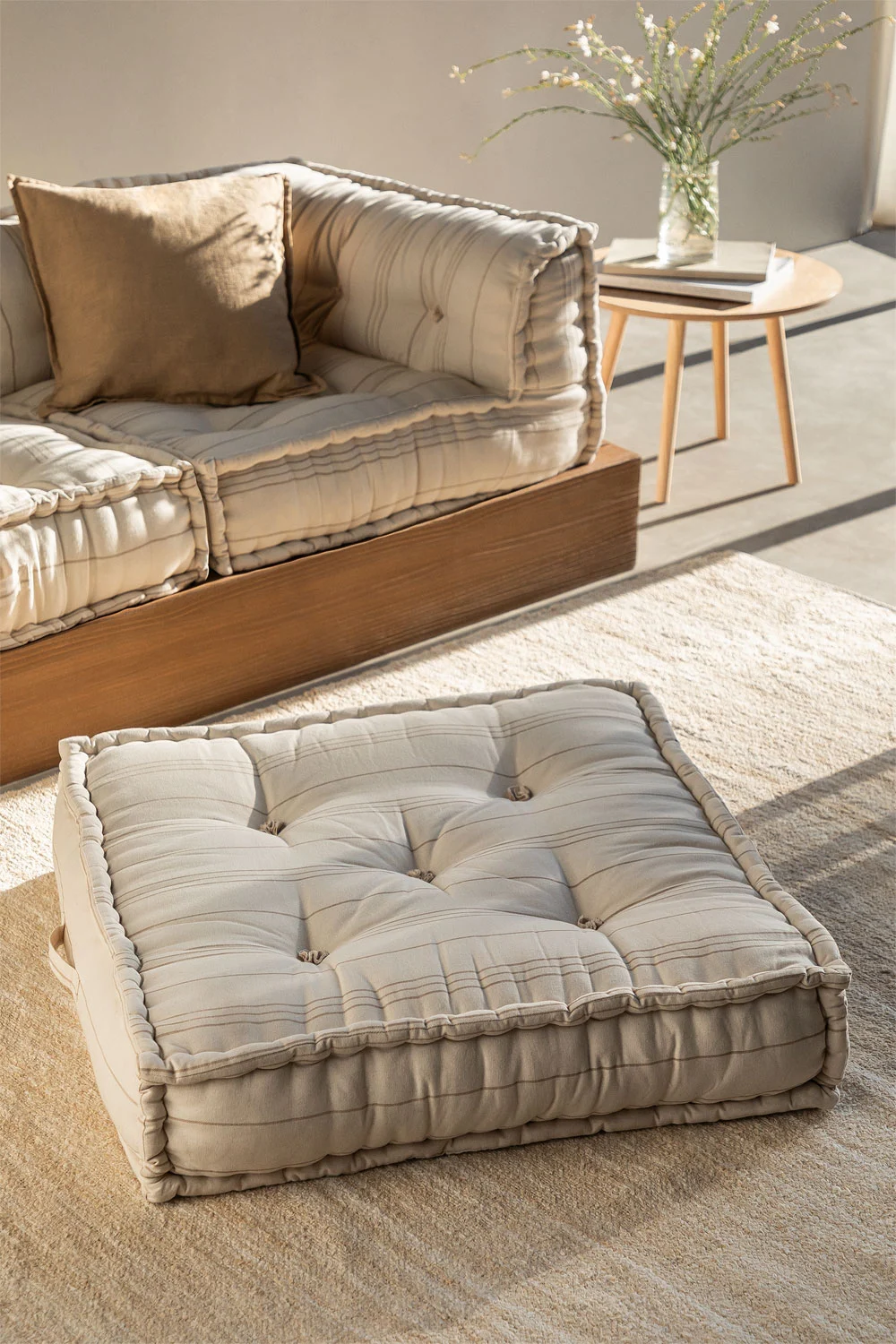 Zona relax su piccola terrazza chiusa con divano basso, pouf imbottito e tappeto in fibra naturale, ideale per creare in pochi metri uno spazio accogliente e rilassante.