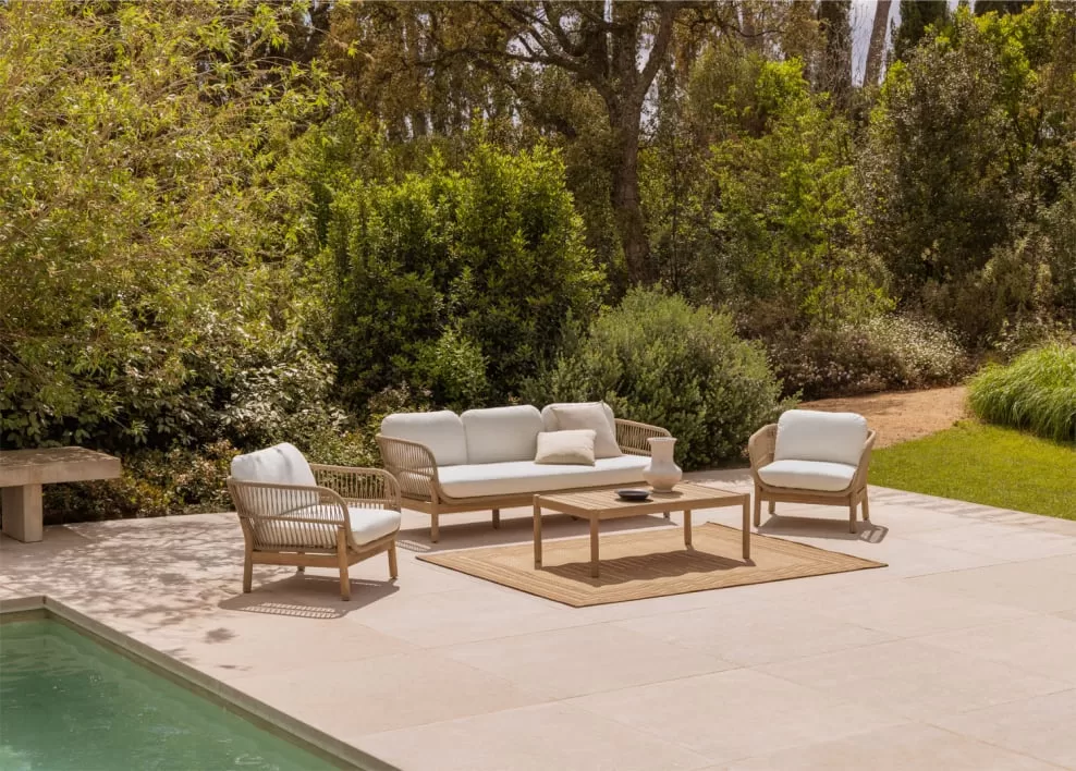 Area relax a bordo piscina con divano e poltrone da esterno su un tappeto da giardino, idea elegante e funzionale per giardini con piscina dallo stile naturale.
