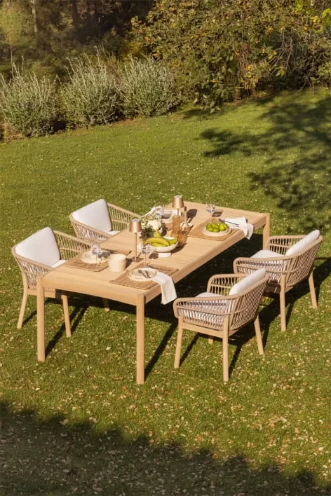 Area pranzo esterna con tavolo in legno chiaro e sedie da giardino intrecciate, ideale come idea per un giardino dallo stile naturale e rilassato.