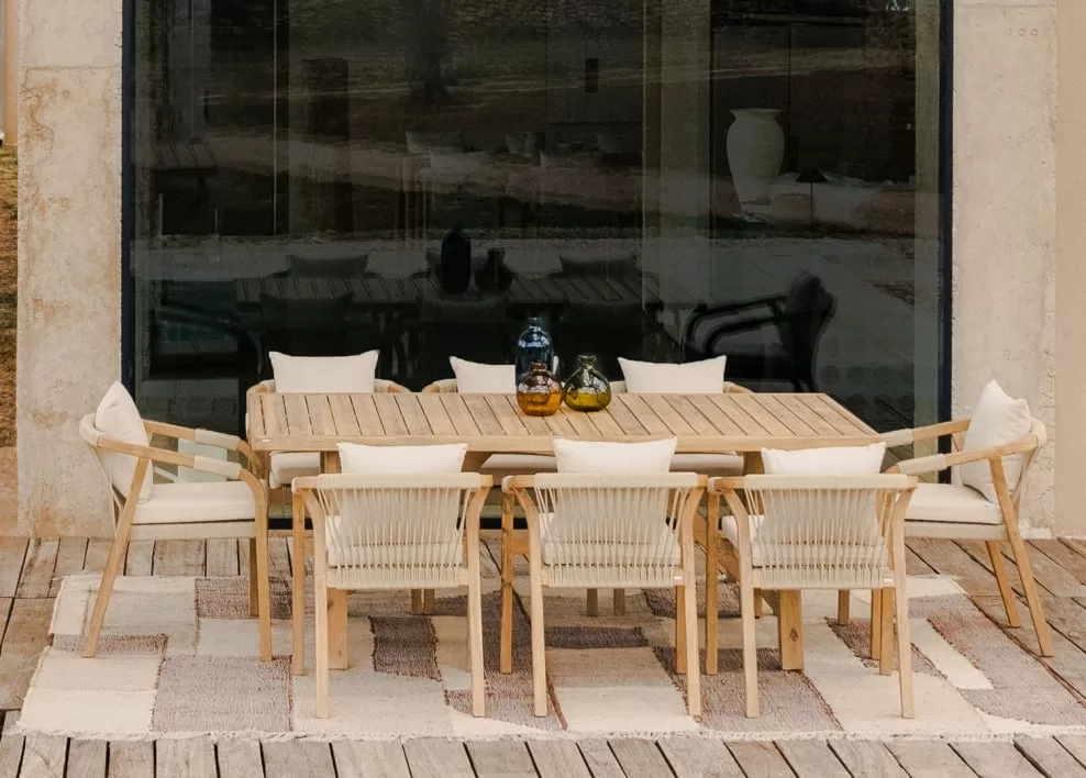 Comedor exterior en terraza chill out con mesa y sillas de madera clara sobre alfombra neutra, ideal para un estilo mediterráneo o minimalista relajado.