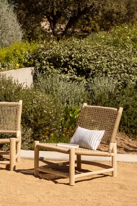 Poltrona da giardino in legno e corda naturale con cuscino decorativo in un ambiente esterno minimalista, ideale per piccoli giardini.