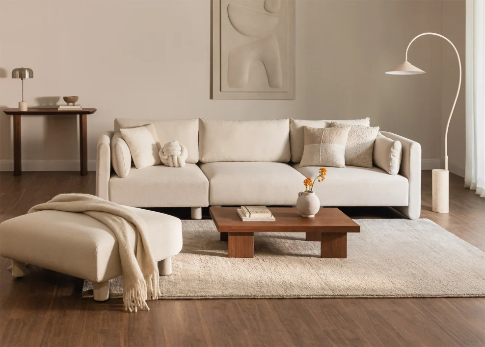 Petit salon fonctionnel et minimaliste avec canapé modulable crème, tapis clair et table basse en bois.