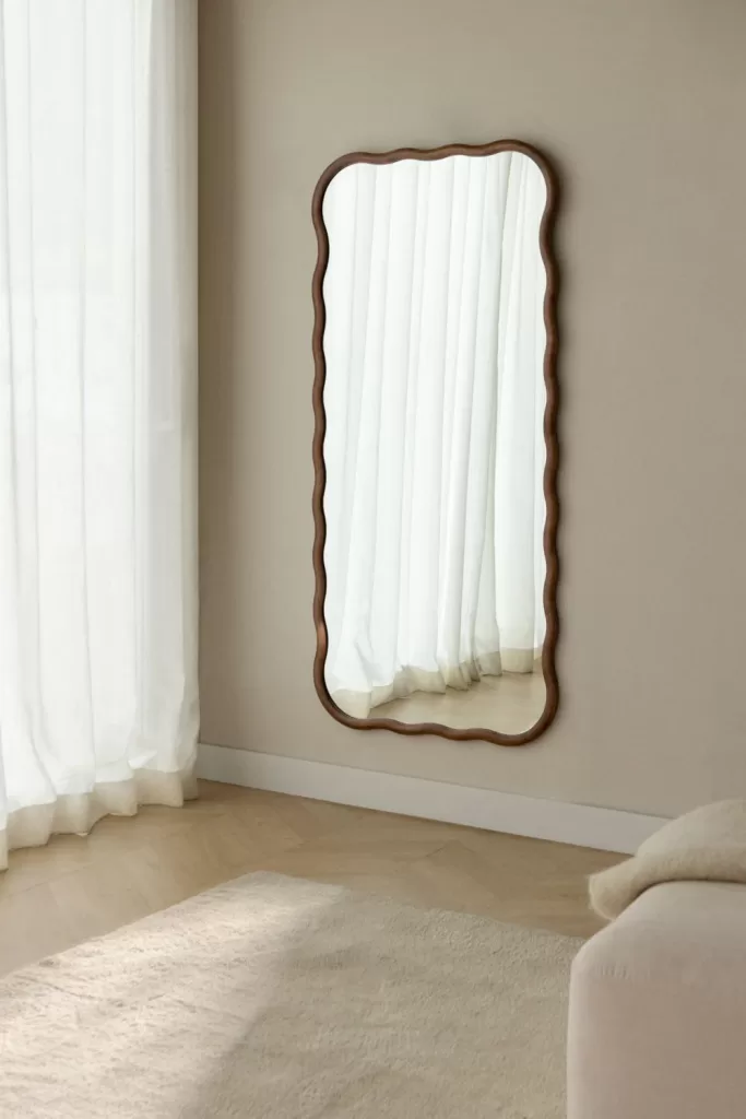 Grande specchio con cornice ondulata posizionato sopra il divano per creare un elegante punto focale in un soggiorno minimalista