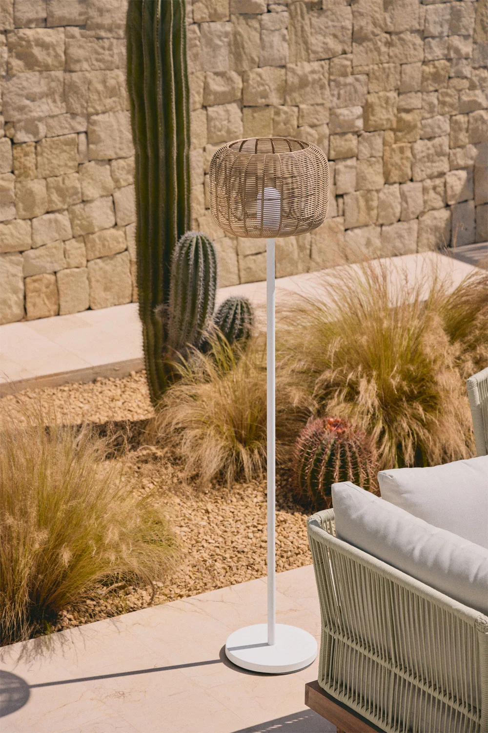 Candeeiro de chão para área exterior em estilo natural ao lado de cactos e mobiliário de jardim, ideal para iluminar pequenos pátios com charme ao entardecer.