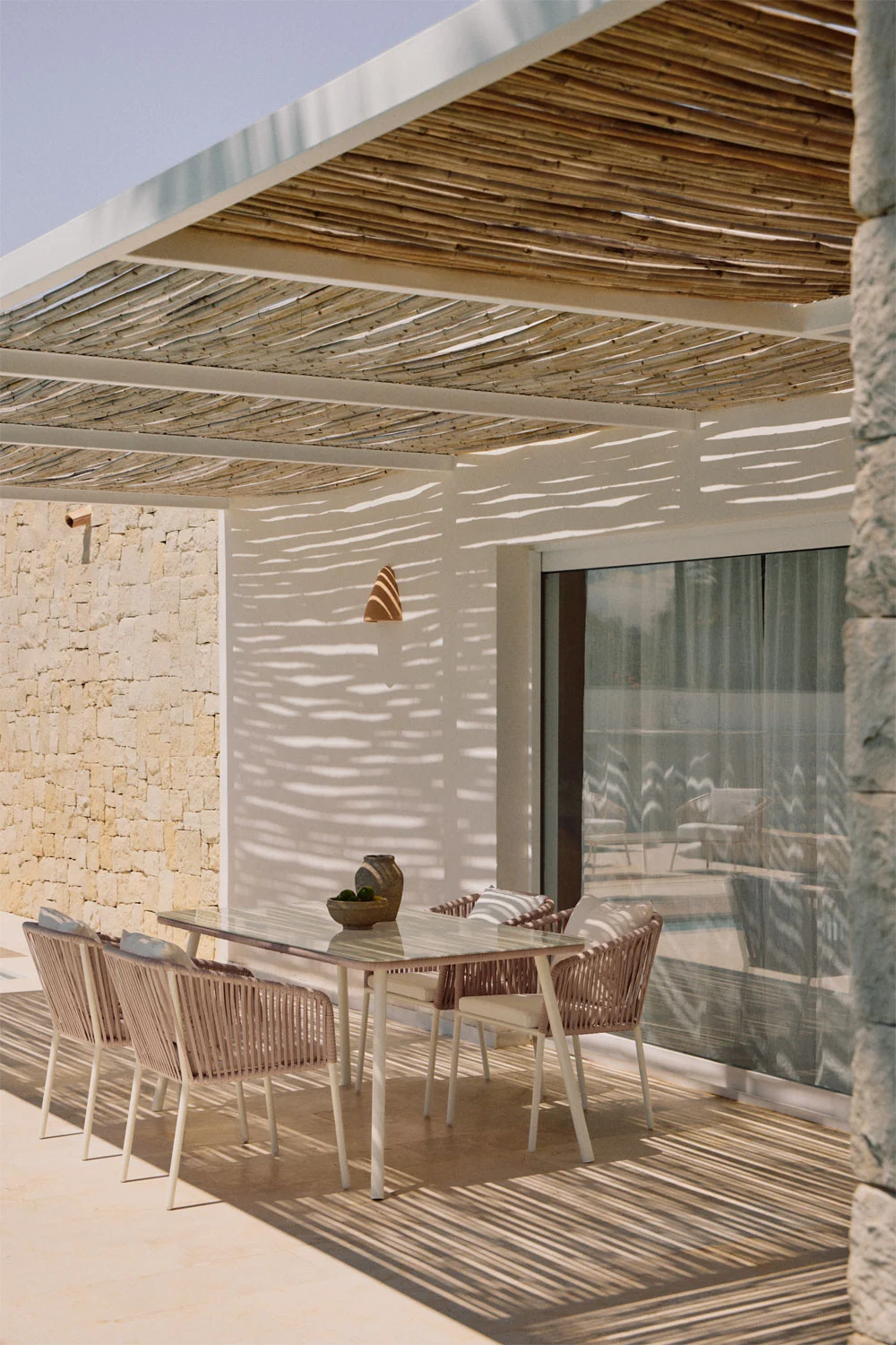 Área de jantar ao ar livre em um charmoso terraço de cobertura, sob uma pérgola de junco que proporciona sombra e elegância mediterrânica.