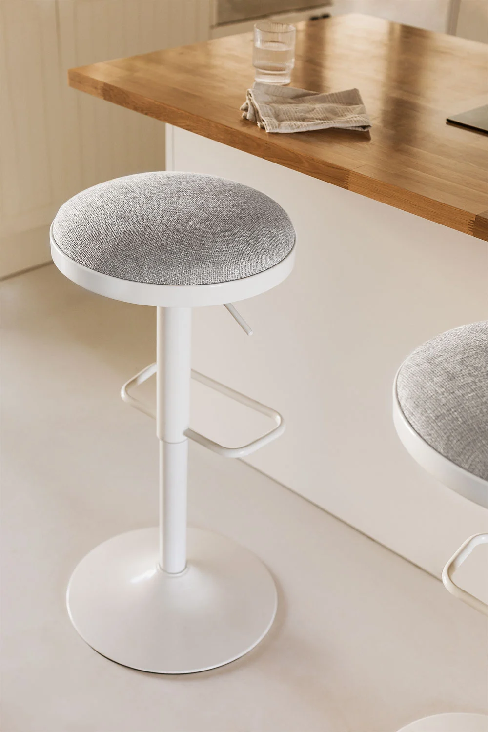 Diseño de cocina pequeña con taburete blanco y gris claro, uso de colores suaves y superficies reflectantes para ampliar el espacio
