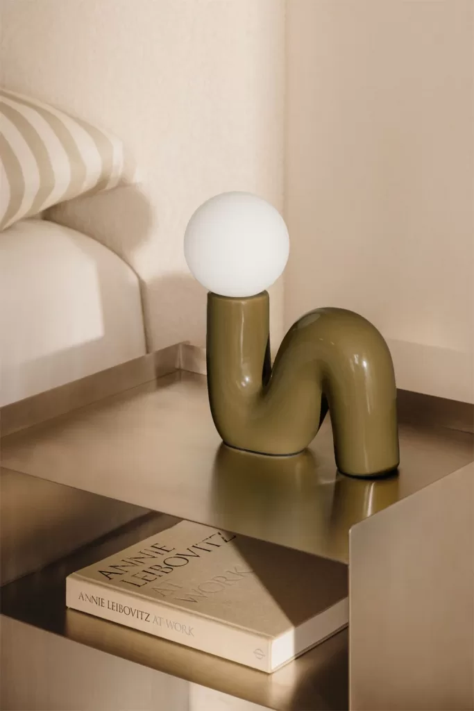 Lampe design sculpturale sur une table de chevet moderne, exemple d'éclairage d'ambiance dans la décoration d'une chambre principale moderne.