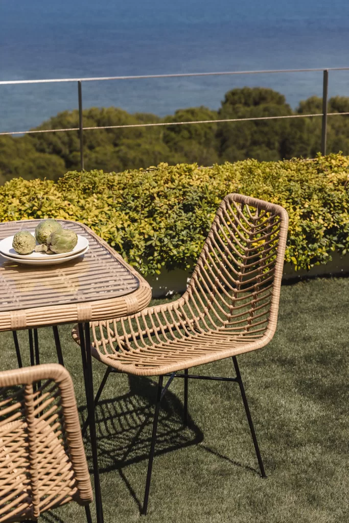 Table et chaises en rotin synthétique avec vue sur la mer, un exemple inspirant de la façon de décorer de grandes terrasses avec des matériaux naturels et un design méditerranéen.