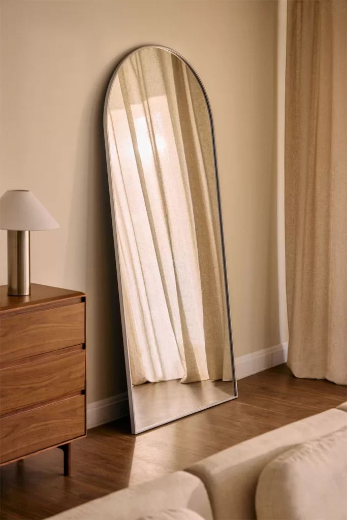 Decoração de sala de estar em cinza e bege com espelho metálico e detalhes aconchegantes, trazendo luz e modernidade ao ambiente.