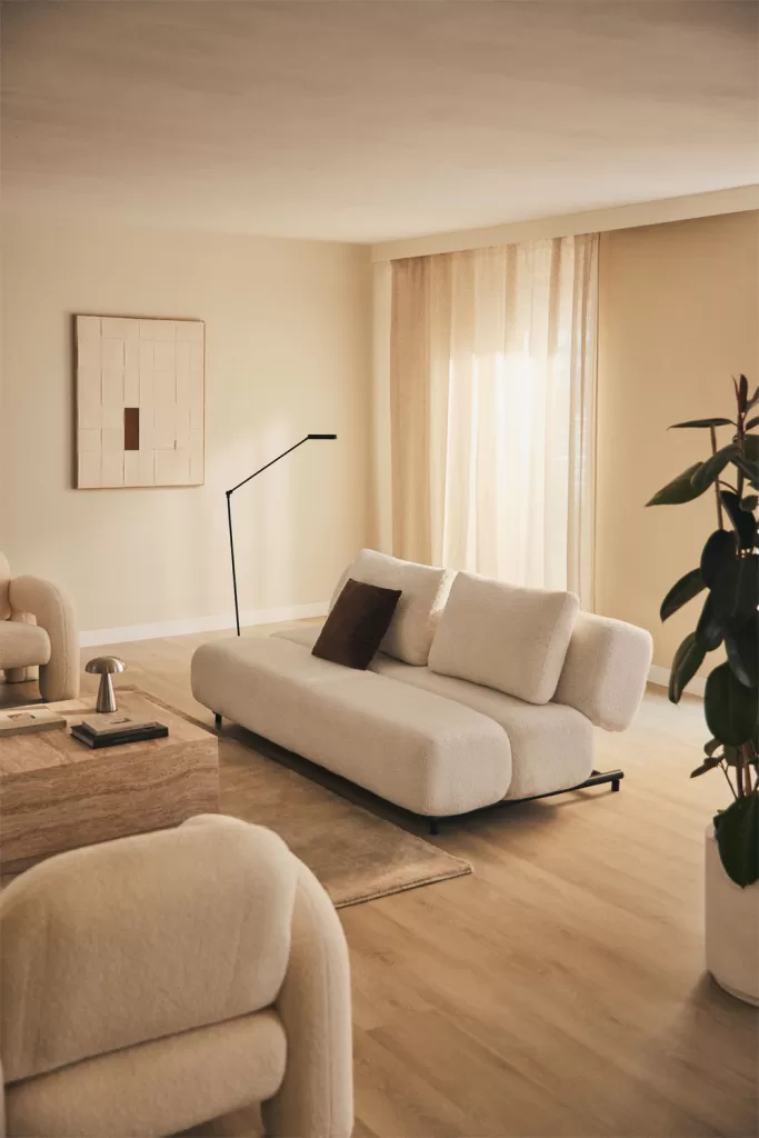 Sala de estar em tons de cinza e bege iluminada por camadas de iluminação com luminária de chão, abajures e luz natural para um ambiente aconchegante
