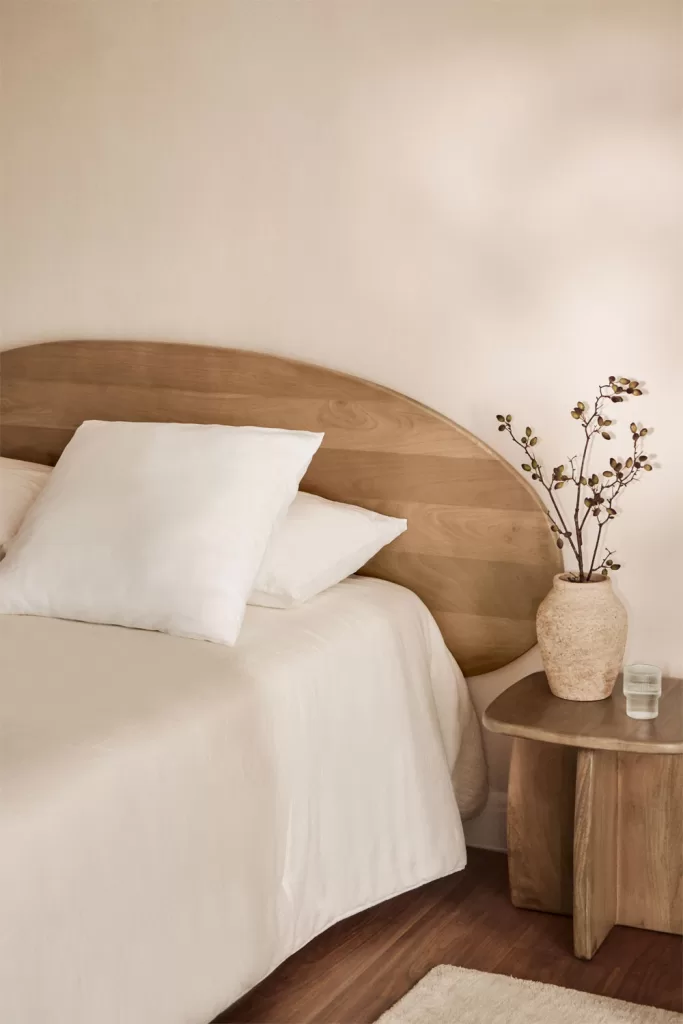 Mur et lit gris doux avec tête de lit incurvée en bois, table de chevet et vase ; chambre sereine grise et bois