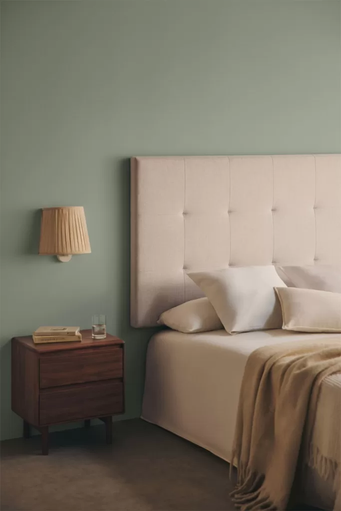 Lit et tête de lit dans une chambre verte et grise, murs aux teintes douces transmettant le calme