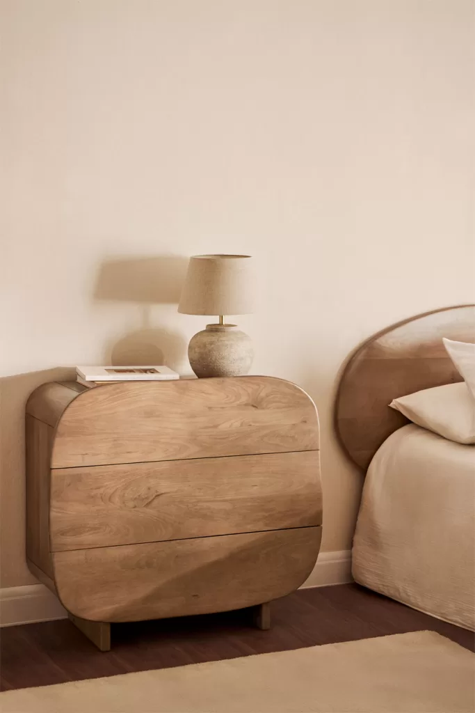 Mesita de noche de madera junto a la cama, contraste cálido en un dormitorio gris y blanco