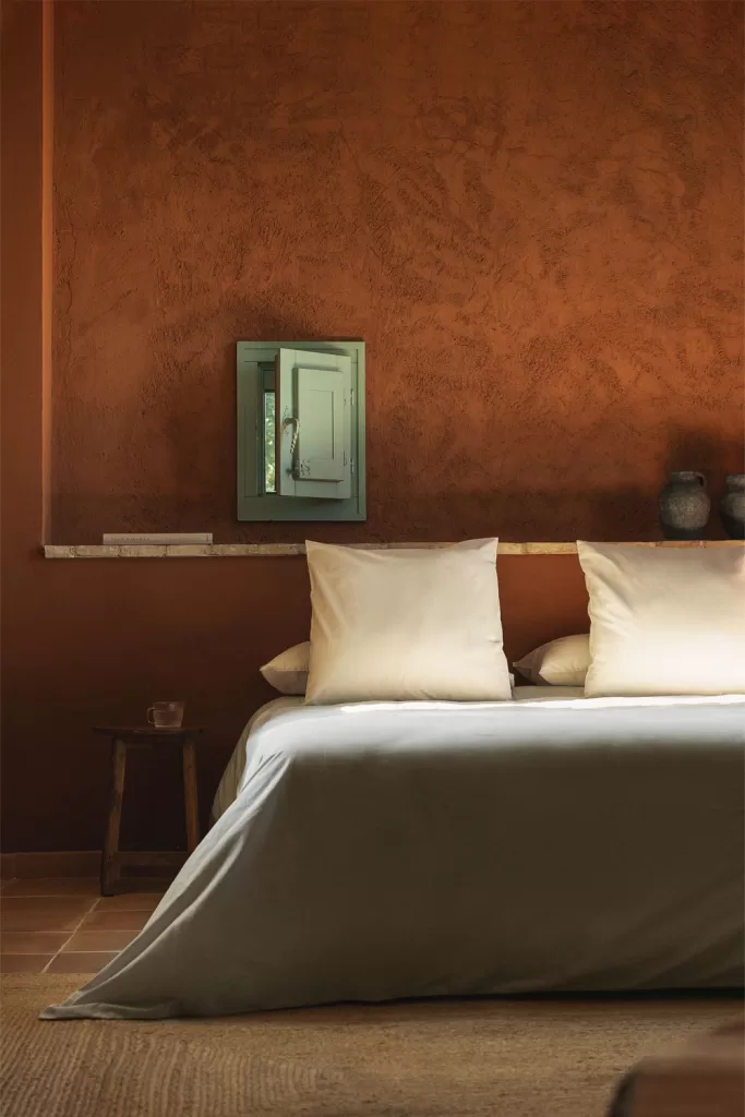 Chambre grise et bois avec mur en stuc terre cuite, literie et linge gris ; ambiance tactile et cosy