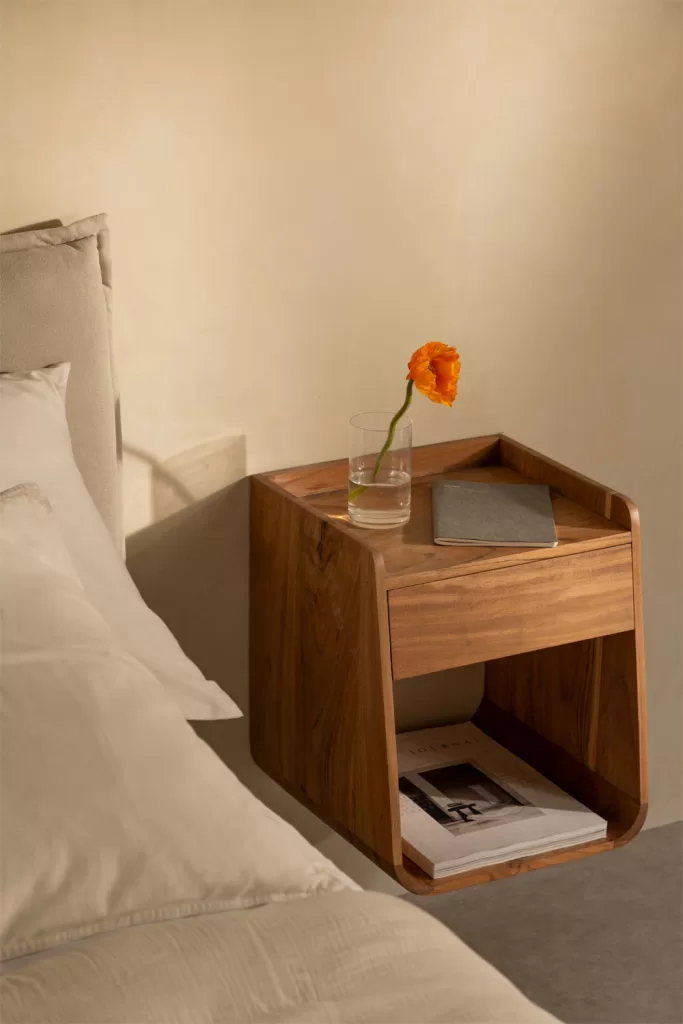 Table de chevet en bois massif avec fleur orange à côté d'un lit gris; accent chaleureux dans une chambre grise et bois