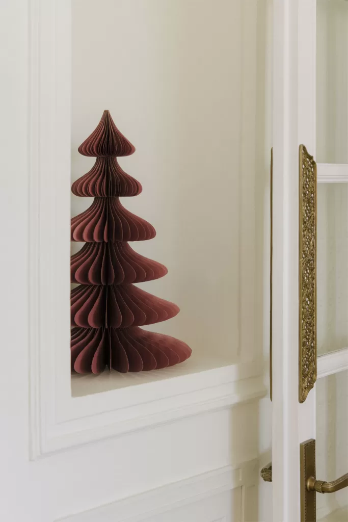 Decoração de Natal minimalista com árvore de papel junto a uma porta, exemplo de elegância em tons neutros para salas pequenas.