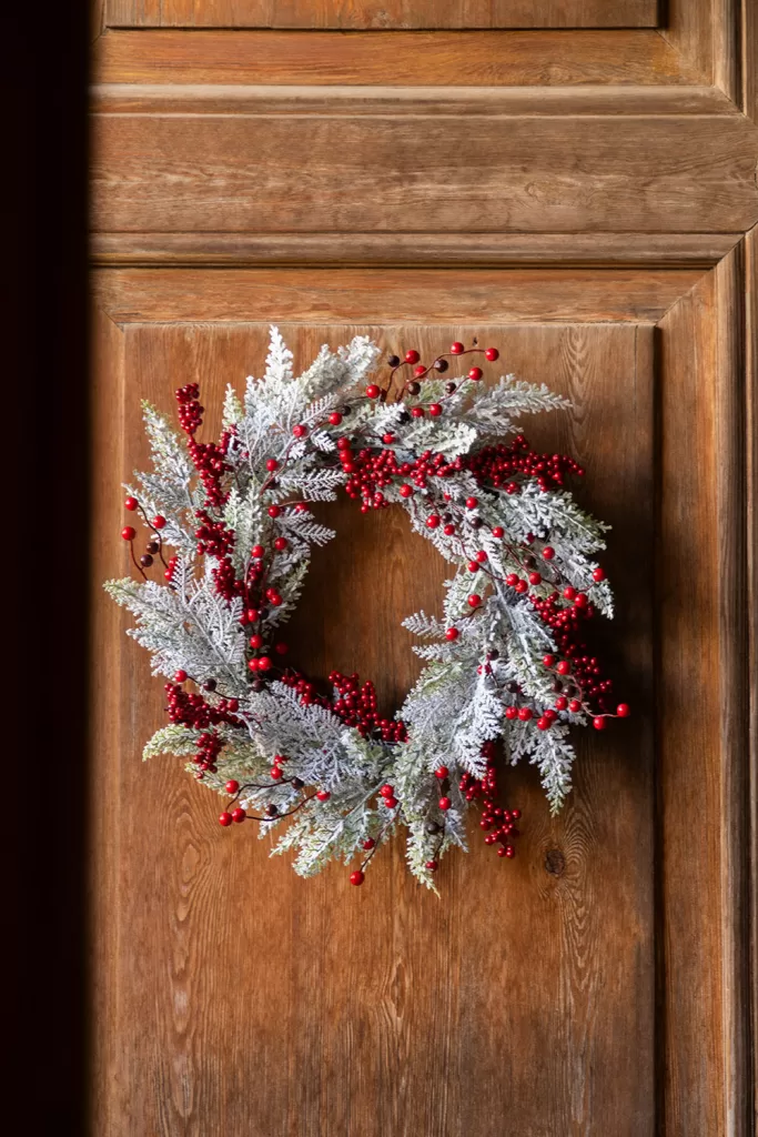 Coroa de Natal pendurada numa porta de madeira, uma excelente forma de decorar sem ocupar espaço no chão numa sala pequena.