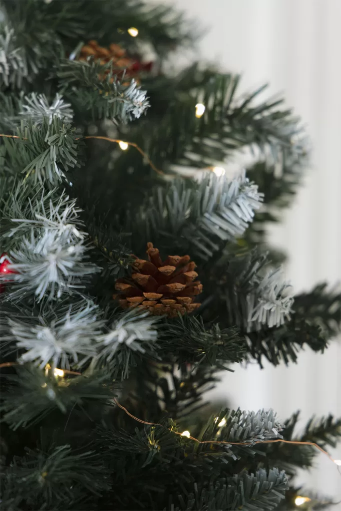 Sapin de Noël artificiel Livigno orné de pommes de pin décoratives et de baies rouges pour un aspect naturel.