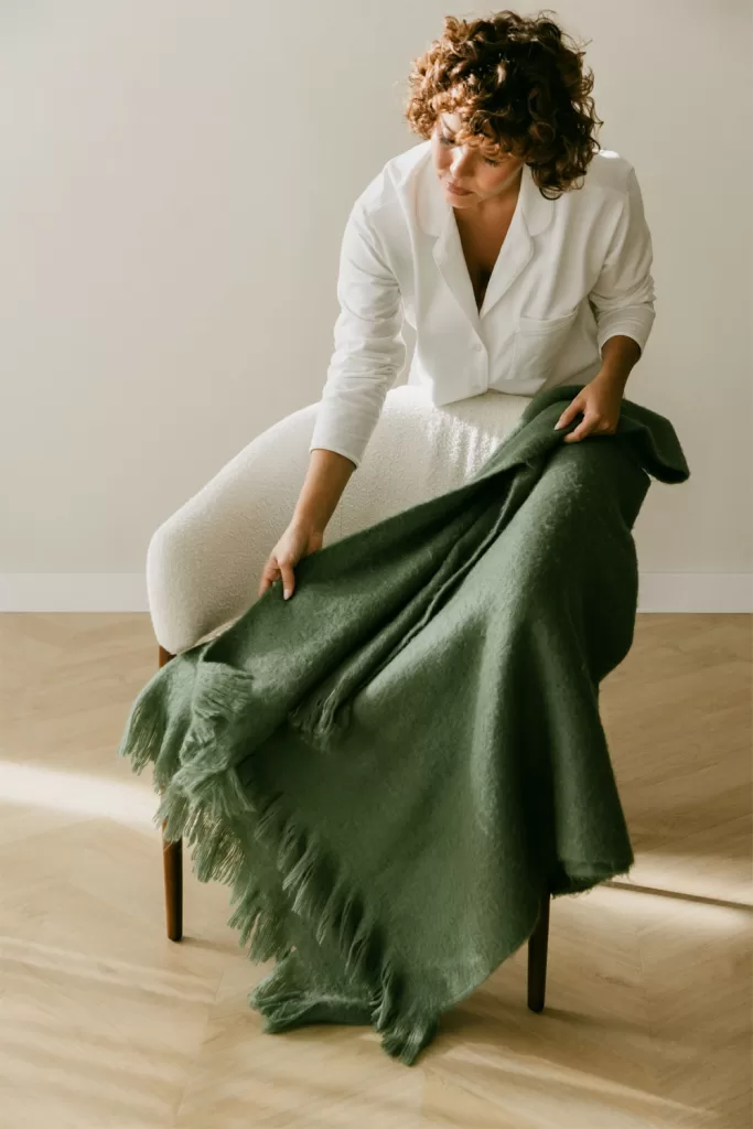 Manta de malha verde-escura sobre um sofá cinza-escuro, exemplificando a combinação com tons frios e profundos.