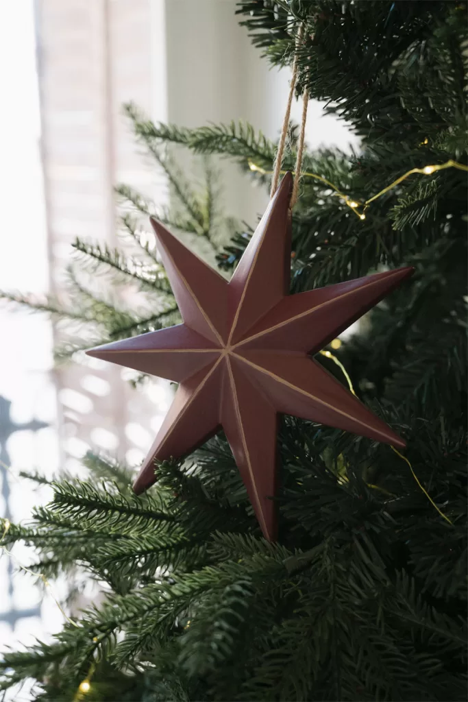 Gros plan sur des décorations de Noël en papier plié et MDF accrochées en profondeur dans le sapin pour créer du relief.