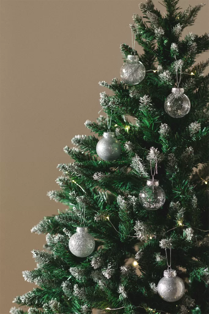 Détail de décorations de Noël Suvy suspendues à une branche de sapin, apportant une touche d'éclat métallique.