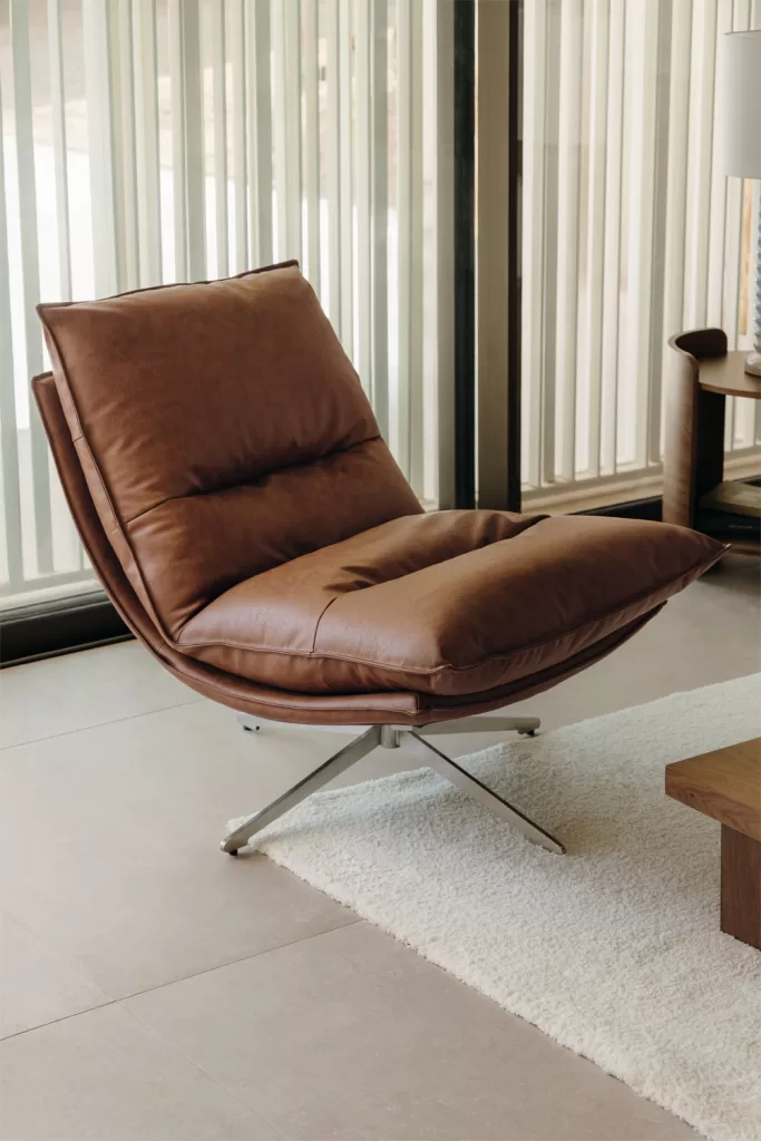 Poltrona giratória em pele cor de mostarda ao lado de um sofá cinza-escuro, criando um contraste quente e acolhedor.