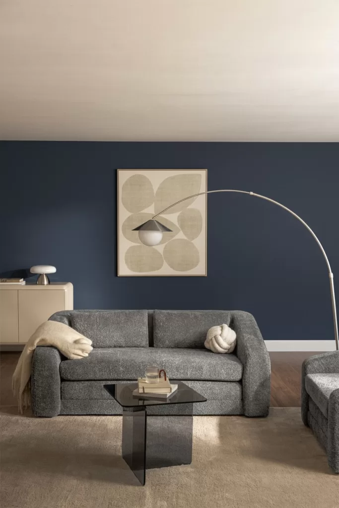 Sala de estar com sofá cinza-escuro posicionado contra uma parede de destaque em azul-escuro.