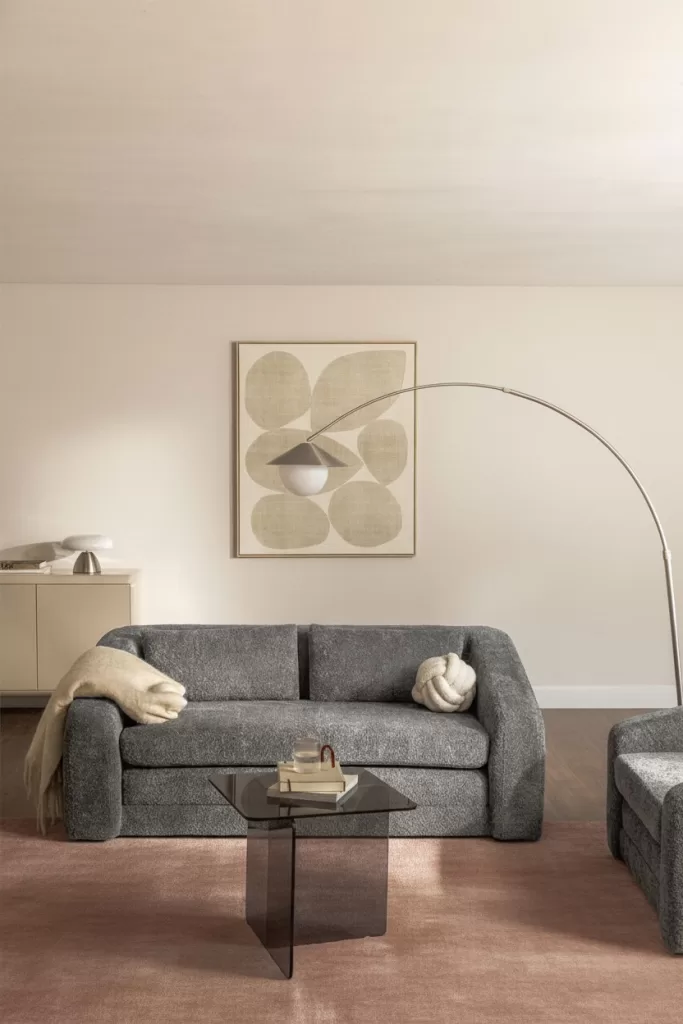 Sala de estar moderna com sofá cinza-escuro, tapete rosa-claro e almofadas a condizer, criando um contraste suave.