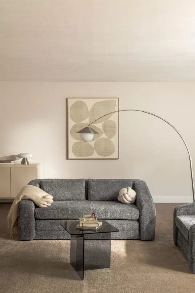 Sofá-cama cinza-escuro em tecido bouclé, complementado por um candeeiro de pé dourado para um toque de luxo.