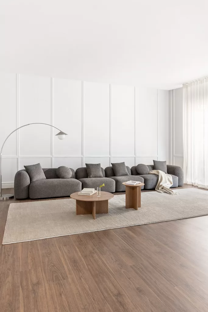Sala de estar minimalista com sofá modular cinza-escuro e têxteis em tons neutros.