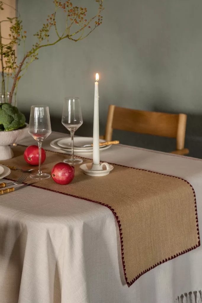 Chemin de table rustique en jute combiné avec une nappe unie comme centre de table de Noël aux textures naturelles.