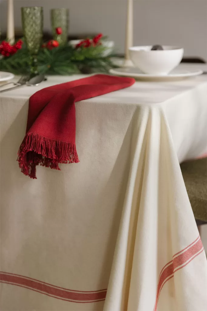 Centre de table de Noël avec nappe couleur crème et détails rouges apportant un style classique et raffiné pour Noël.