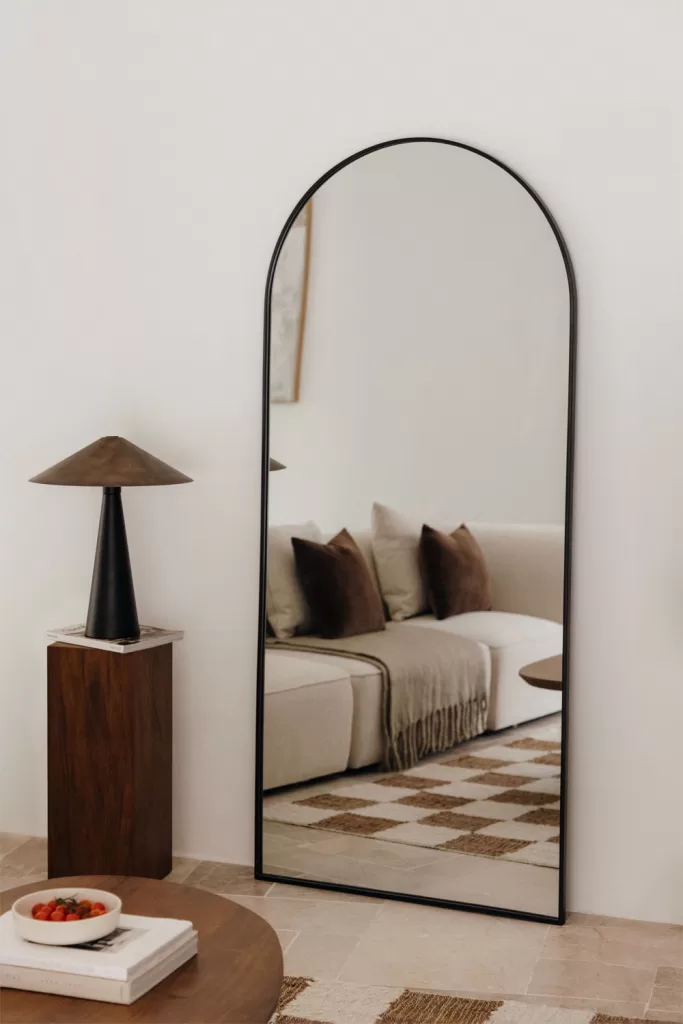 Estilo moderno con espejo de arco negro sobre pared blanca, dormitorio neutro con textiles beige y madera oscura