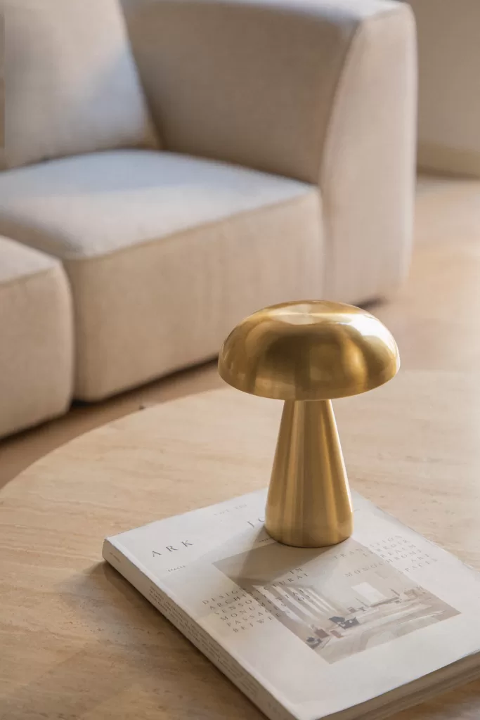 Quarto azul e cinzento com candeeiro de mesa dourado metalizado sobre um livro, sofá bege e detalhes modernos e elegantes.