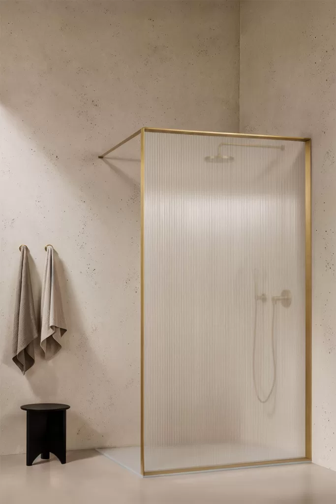 Détail d'une paroi de douche fixe en verre cannelé avec des profilés dorés, dans une salle de bains élégante et lumineuse.