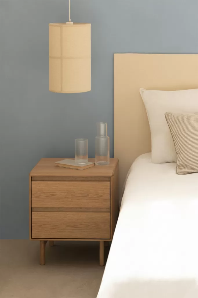 Quarto azul e cinzento com mesa de cabeceira em madeira clara e parede azul-suave, candeeiro suspenso bege e estilo nórdico tranquilo.