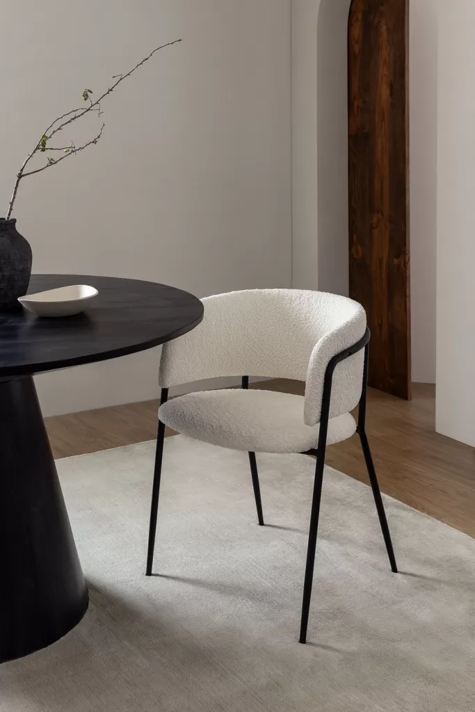 Estilo moderno con mesa redonda negra y silla bouclé blanca, contraste de materiales en comedor luminoso