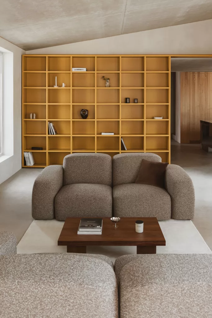 Sofá modular beige y estantería mural de líneas bajas y geométricas en salón amplio de Estilo minimalista