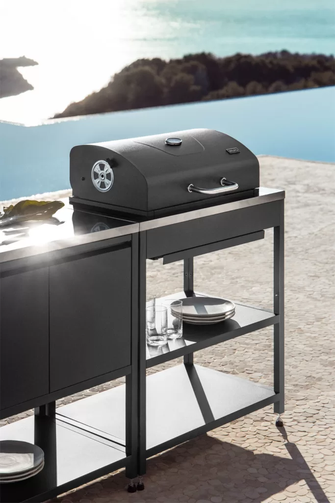 Außenküchenmodul mit schwarzem Holzkohlegrill und minimalistischem Metalldesign vor Meereskulisse