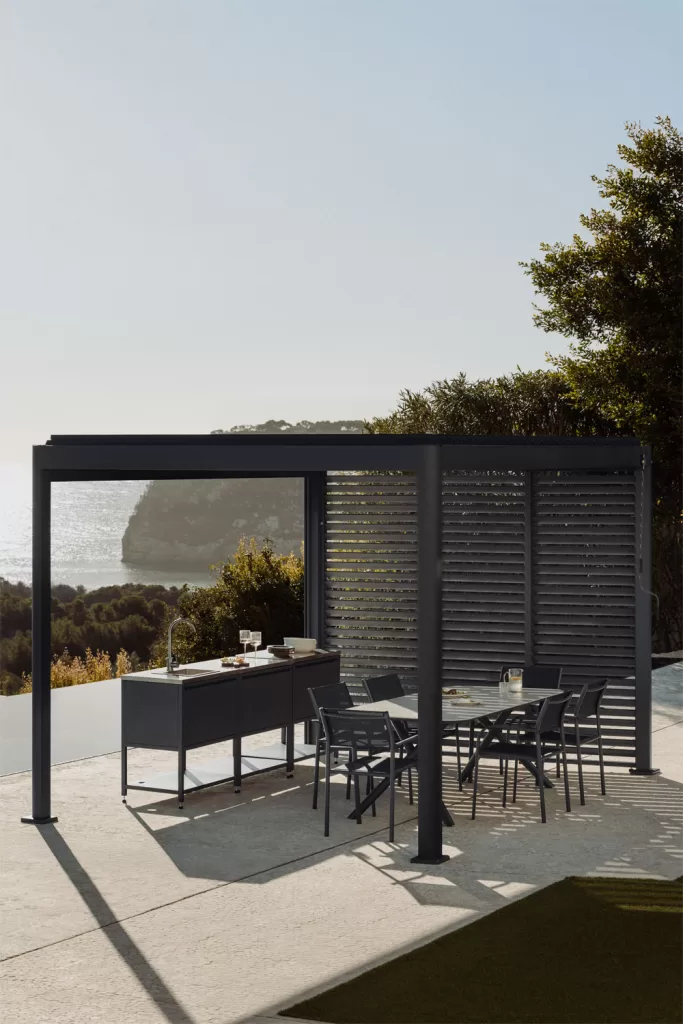 Pérgola bioclimática em alumínio cinza com painéis laterais sobre uma área de refeições exterior.