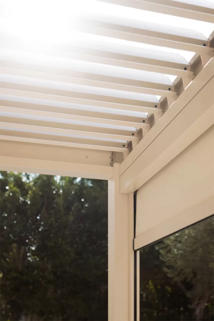 Pérgola bioclimática com lâminas orientáveis em alumínio bege, proporcionando ventilação natural num terraço moderno.