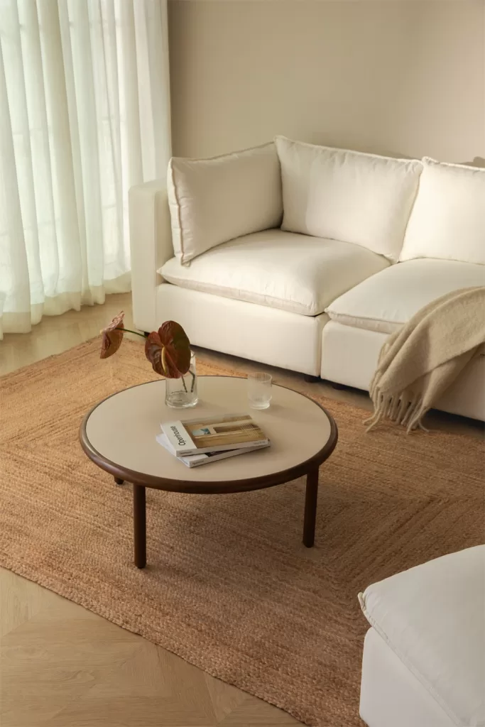 Mesa redonda e tapete de juta com um sofá claro e detalhes em fibras naturais, inspiração para decorar um pequeno apartamento de praia.