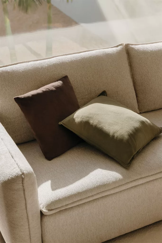 Sofá bege com almofadas de linho e algodão em tons neutros, opções de tecidos frescos para decorar um pequeno apartamento de praia.