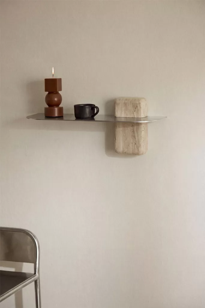 Prateleira flutuante minimalista com velas e têxteis numa parede clara, uma solução vertical para decorar um pequeno apartamento de praia.