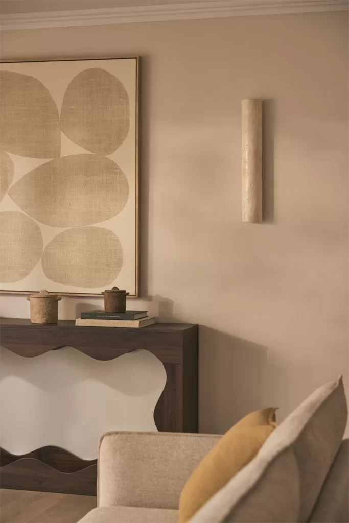 Apliques de parede dourados numa parede bege com uma consola de madeira, perfeitos para a iluminação de uma sala sem teto falso.