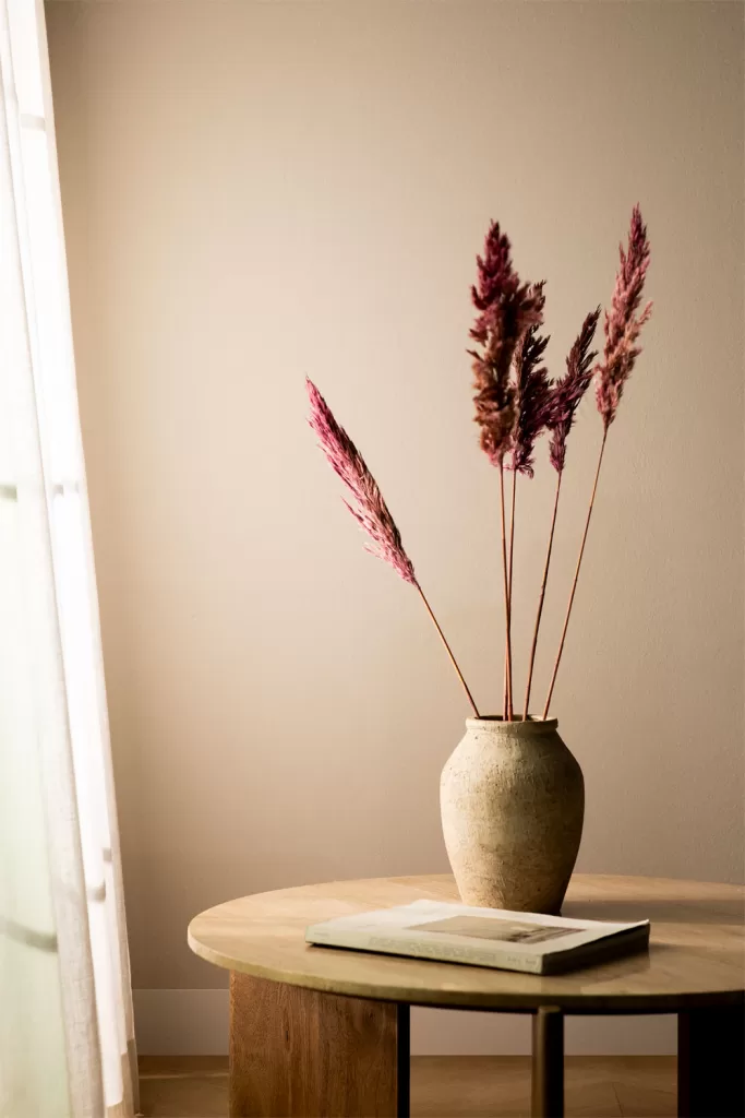 Jarrón con ramas secas sobre mesa de madera, inspiración de como decorar una vitrina de cristal con calidez