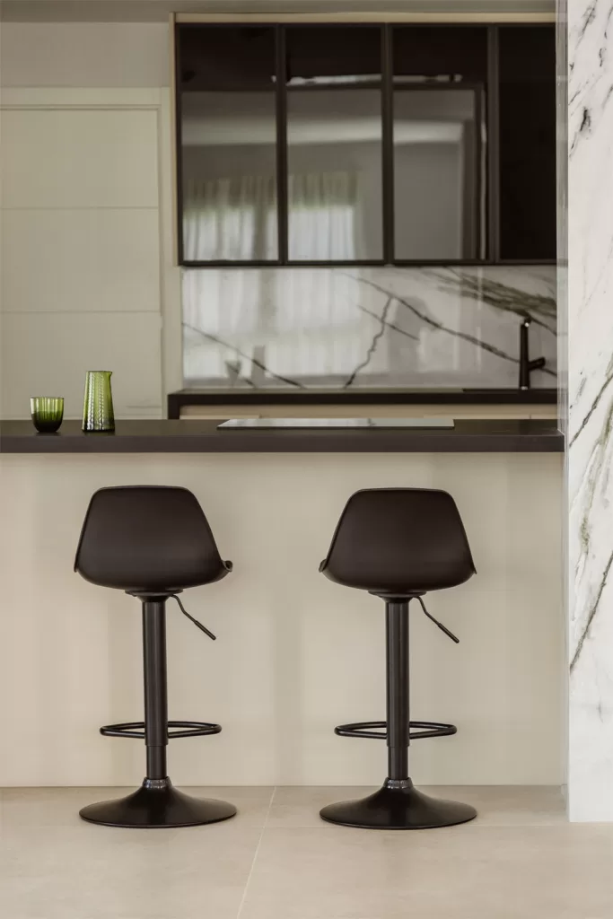 Moderne zweifarbige Küche mit weißer Marmorarbeitsplatte, dunklen Unterschränken und schwarzen Barhockern