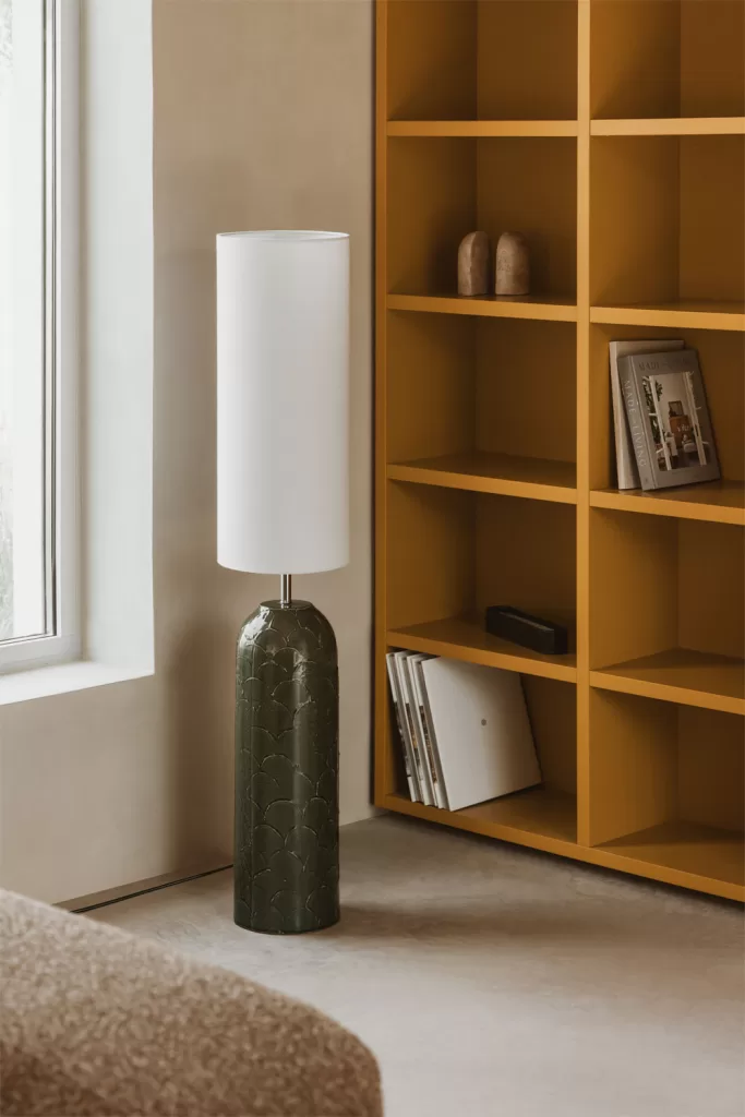 Como decorar um loft com candeeiro de pé branco, estante mostarda e sofá junto à janela