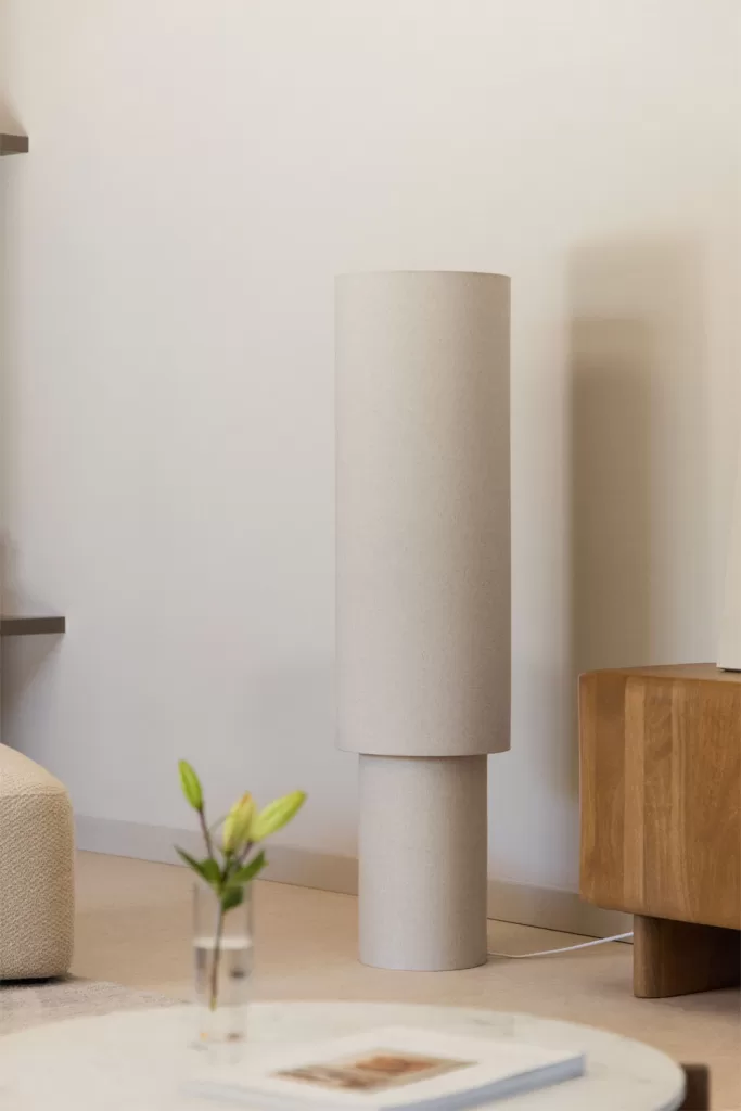 Lámpara cilíndrica cálida sobre mesa auxiliar en salones marrones y beige con luz por capas